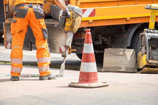 Construction worker using jackhammer beside traffic cone on urban street