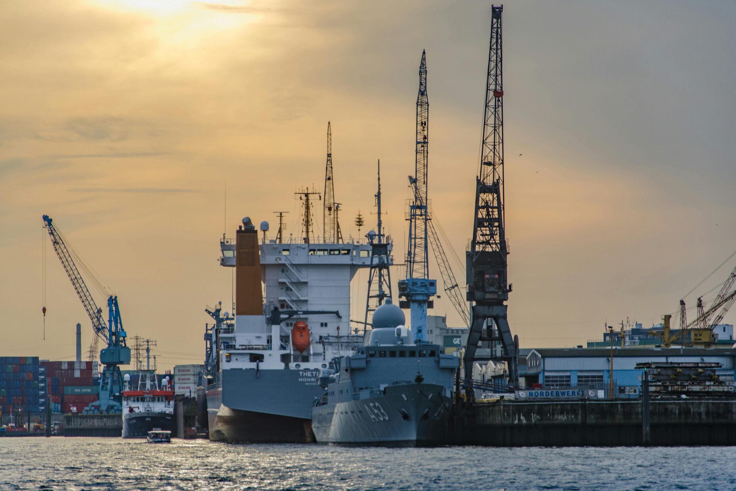 Cargo port scene with ships and cranes at sunset, showcasing industrial and maritime activity.